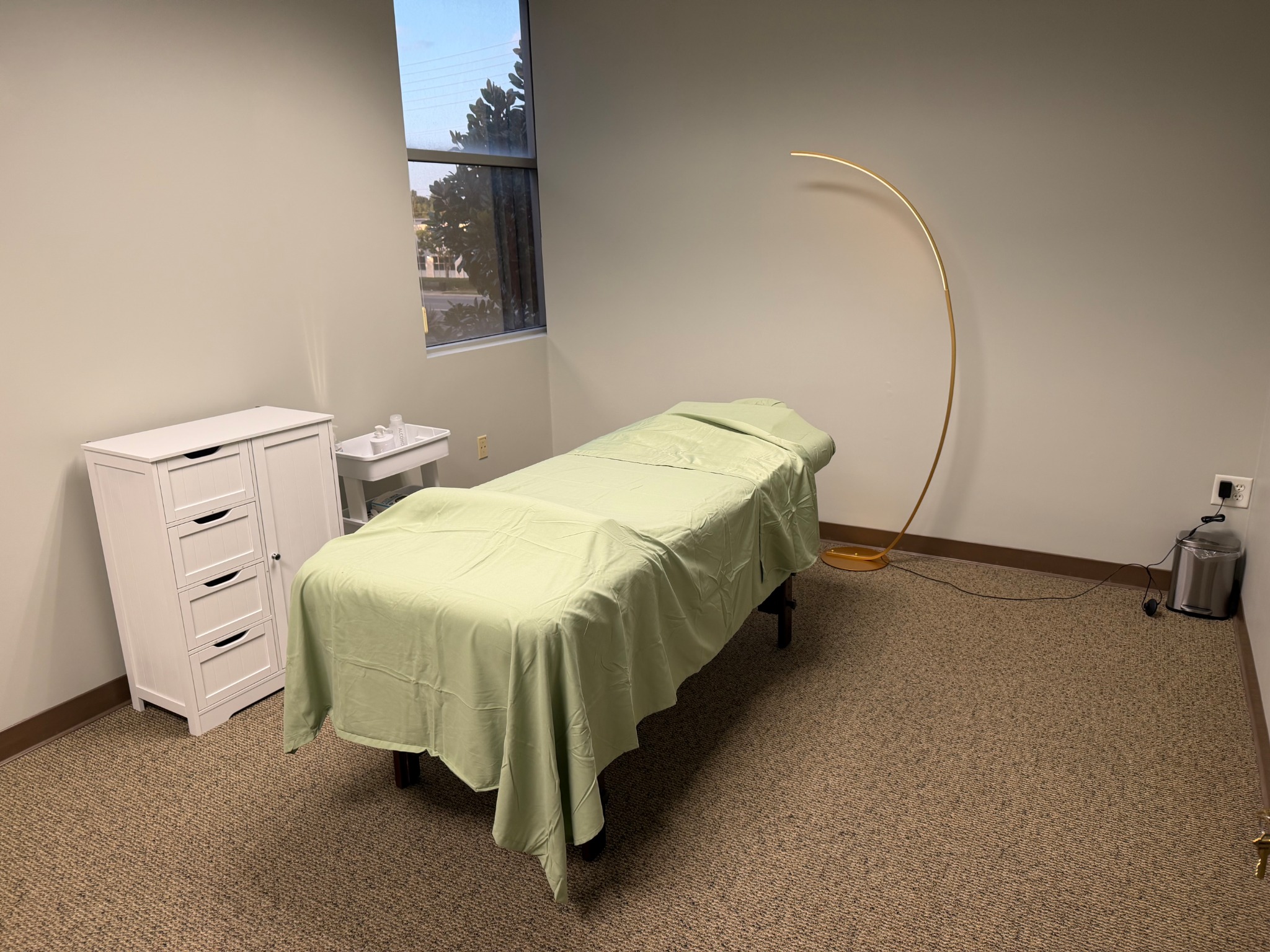Treatment room with a green-covered bed and curved gold lamp