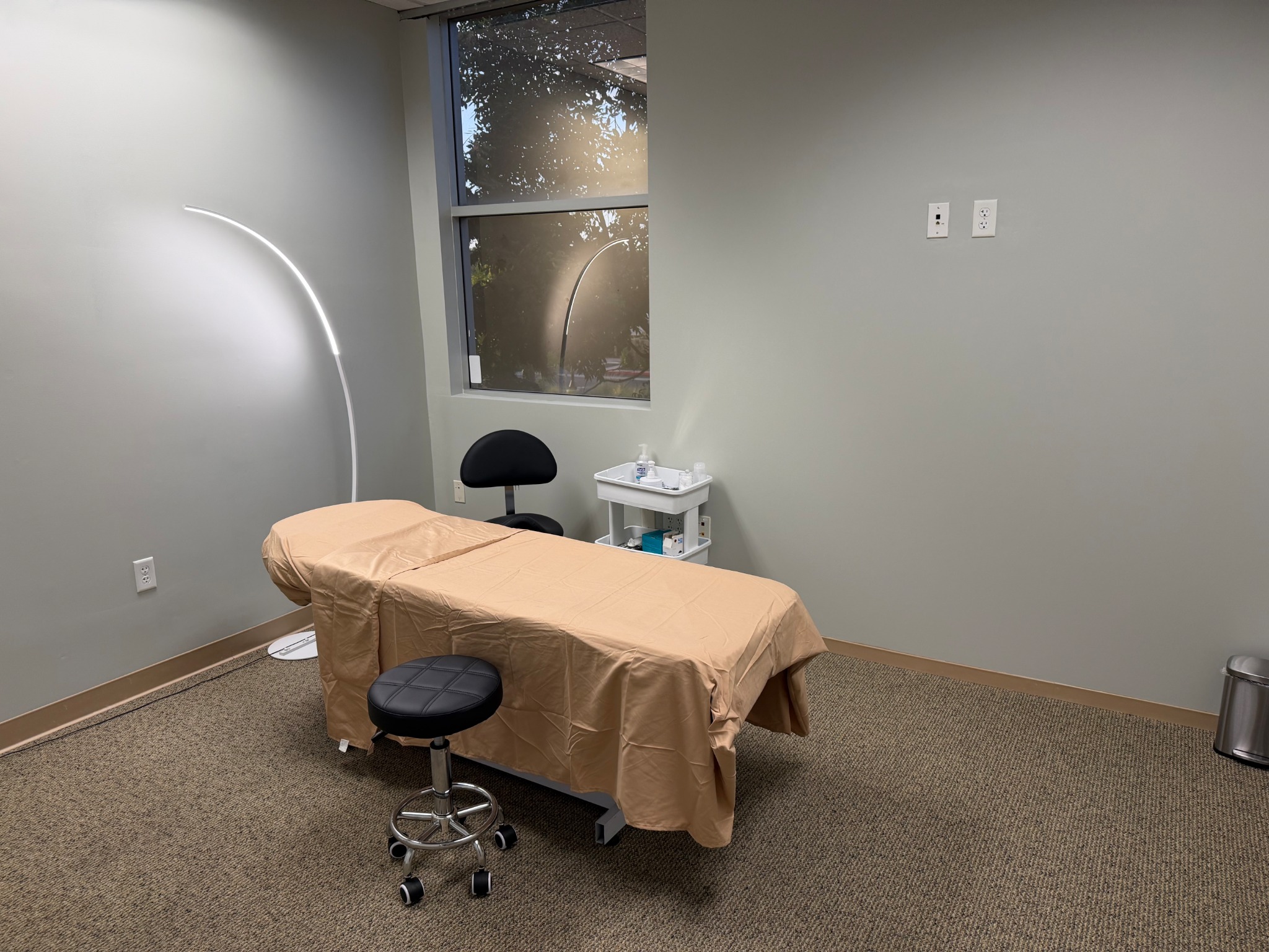 Treatment room with a tan-covered bed beside a window